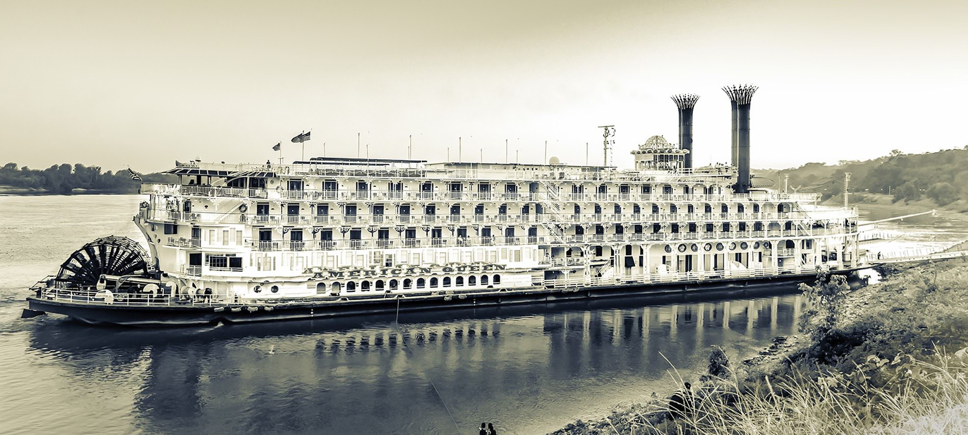 Large, intricate ship sitting on the water with the name American Queen in sepia tones