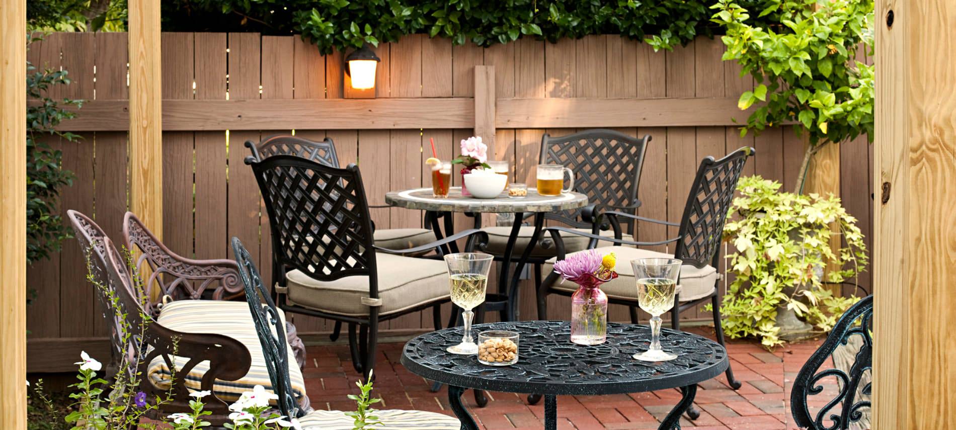 Porch area decorated with dark cast iron furniture, red brick flooring, light brown fencing, and beige cushions; tables coveredin delicious drinks and snacks