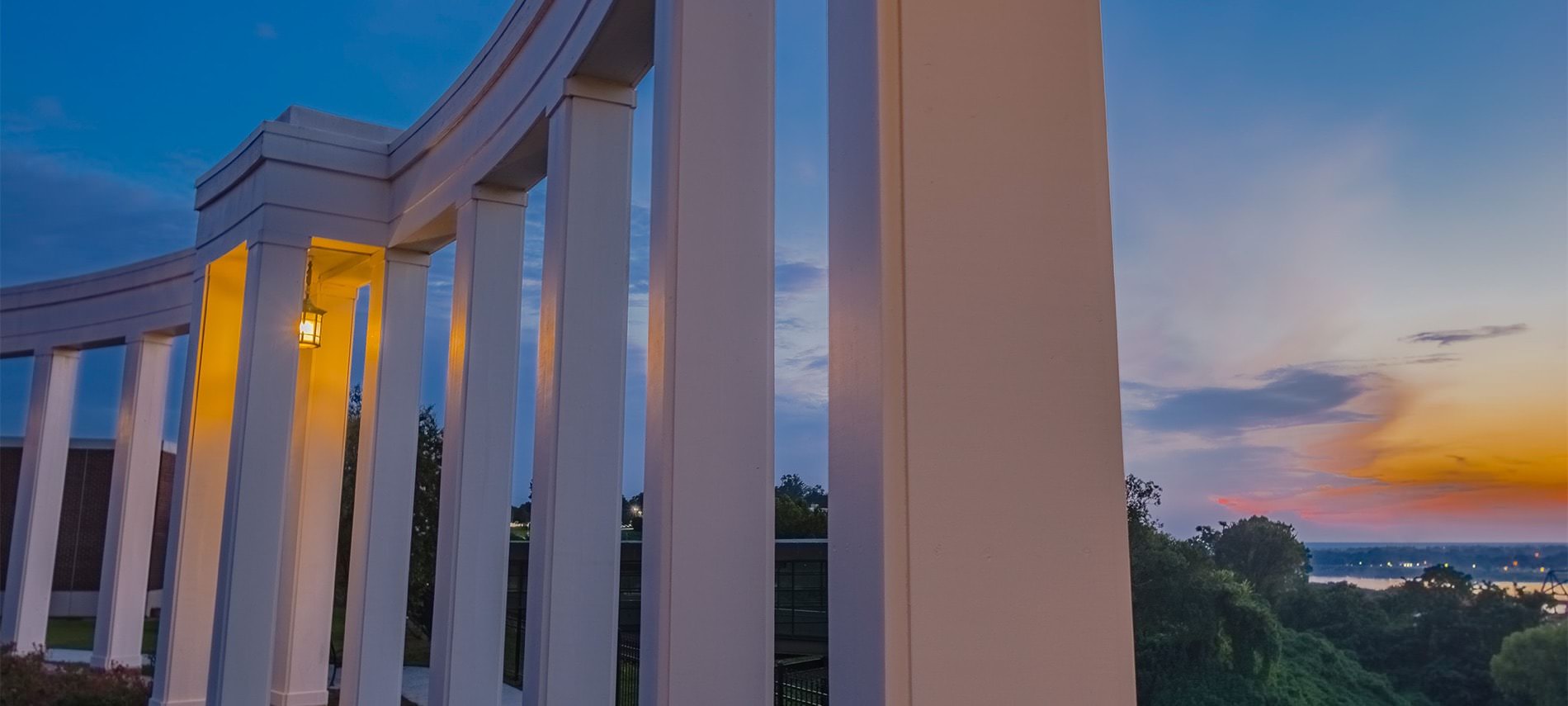 A structure of pillars with a hanging lantern overlooking the water during a beautiful orange sunset