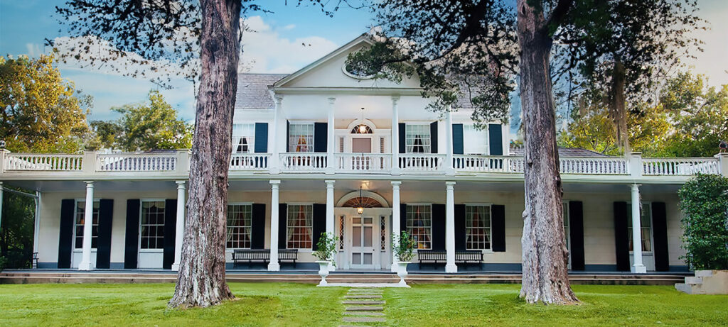 A stately multi story white manor with a large green grass yard