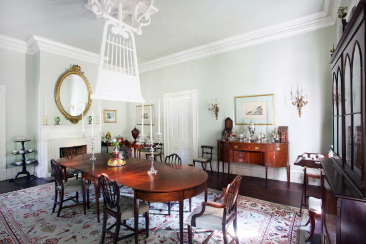 A dining room with a large oval table, wood and cushioned chairs, an antique sideboard and china cupboard, and a tapestry area rug.