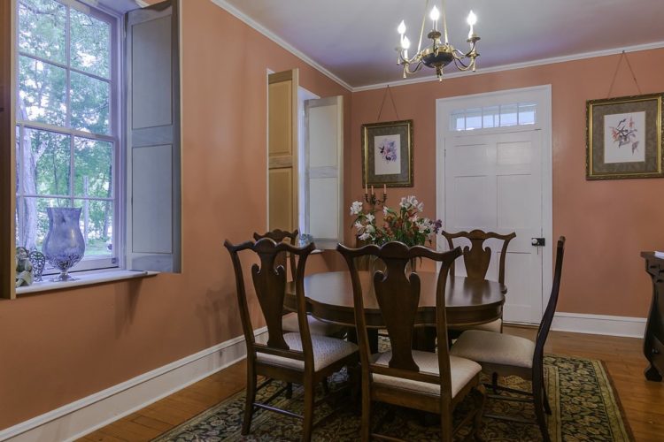 View of dining area decorated with dark wood furniture and cabinetry, salmon walls, wood flooring and a flower patterned rug, and two windows and one door