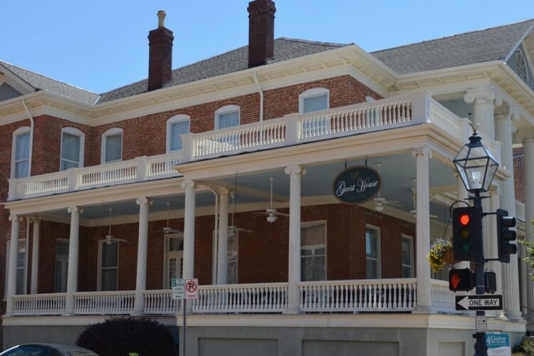 Street view of large, two-story guest house with white pillars and red brick siding surrounded by large porch areas