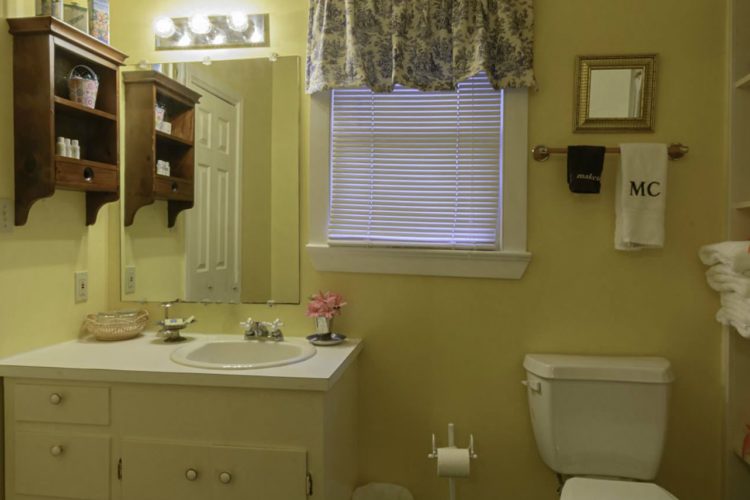 Bright lemon yellow bathroom with towel shelf, toilet, sink with drawers, another closed door, and single window