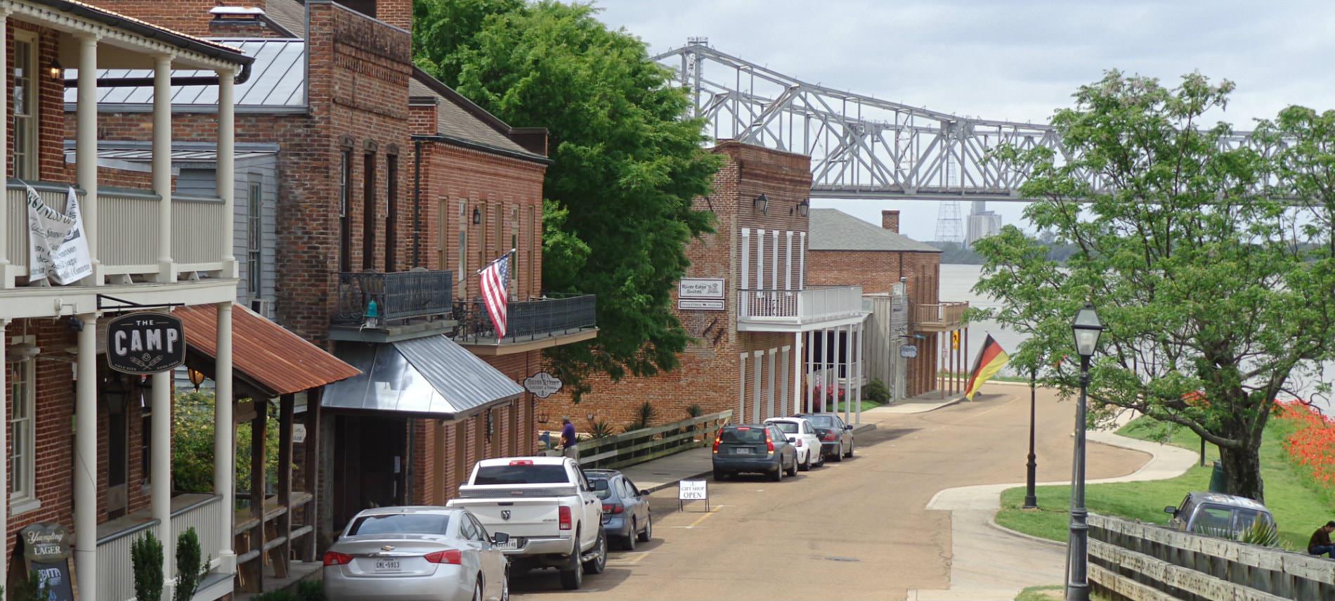 Red brick buildings with store fronts next to a river and bridge