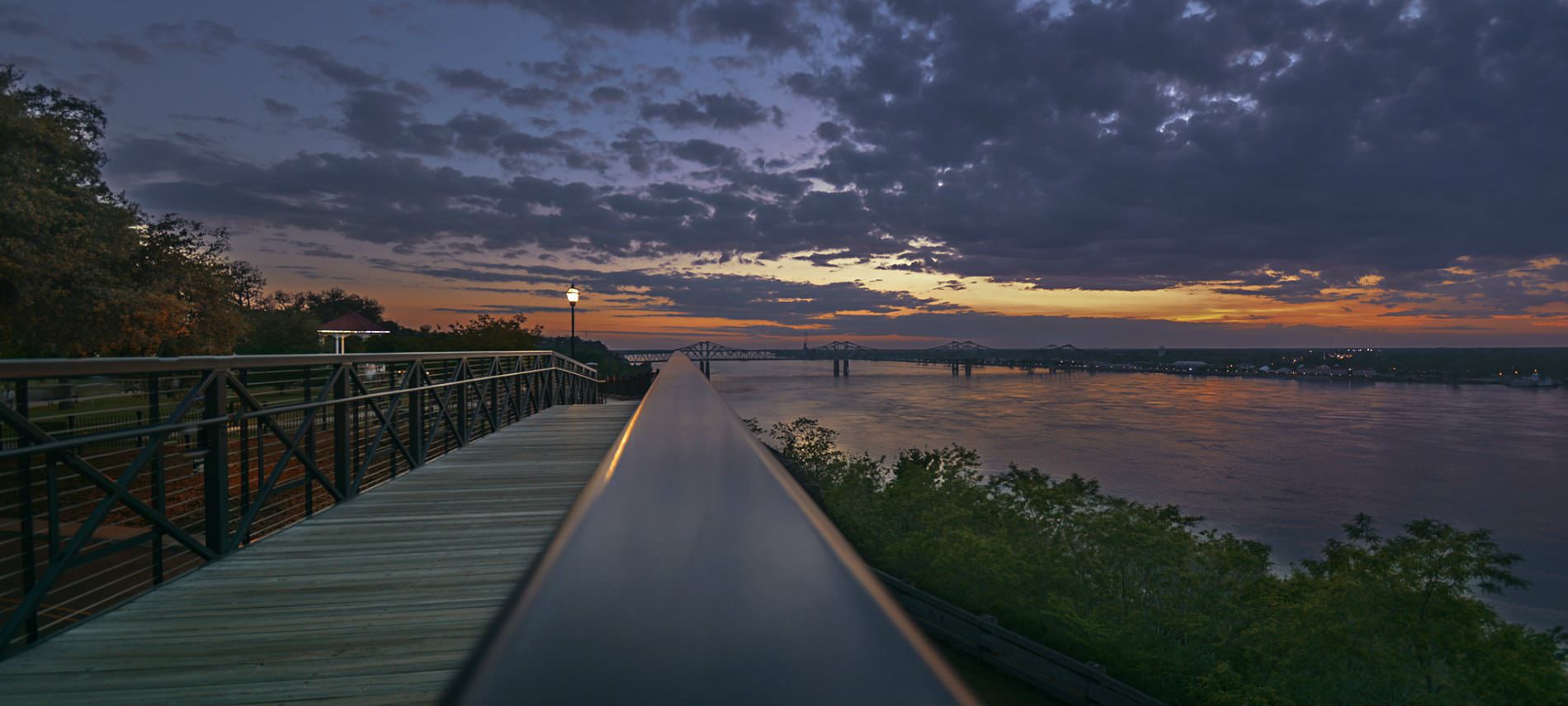 Dark night sky with clouds near dusk next to a river, bridge, and walking path